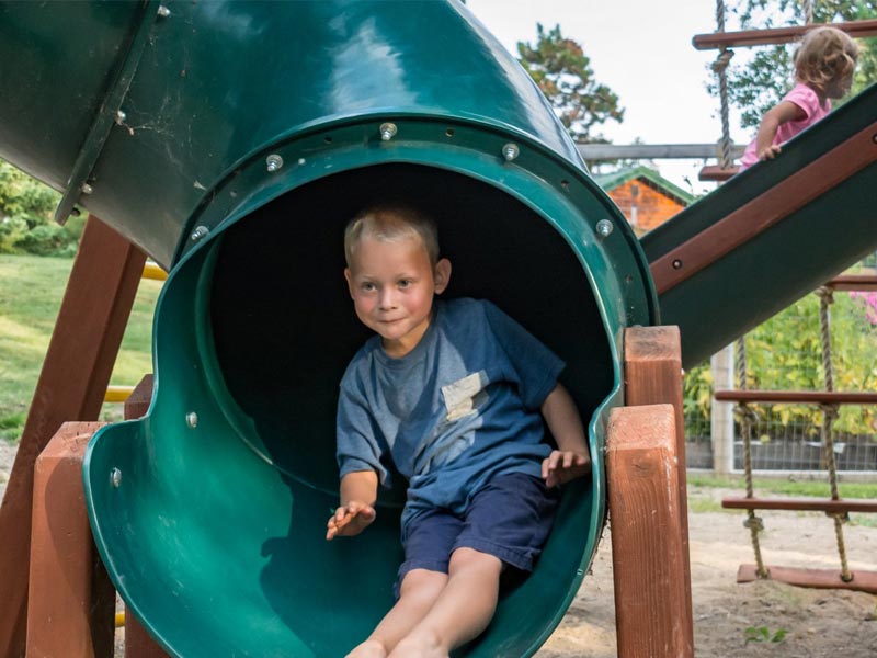 Young boy sliding down green playground tube slide